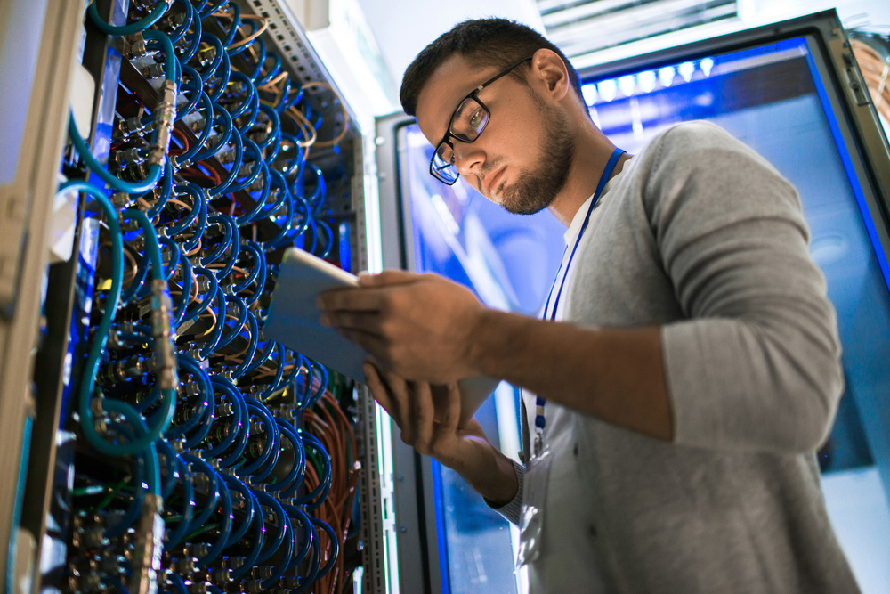 Young network engineer looks at tablet in front of server rack - outsourcing IT post